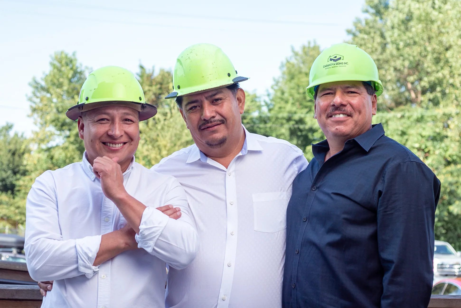 The three owners of Casanova Siding in hard hats, smiling at the camera